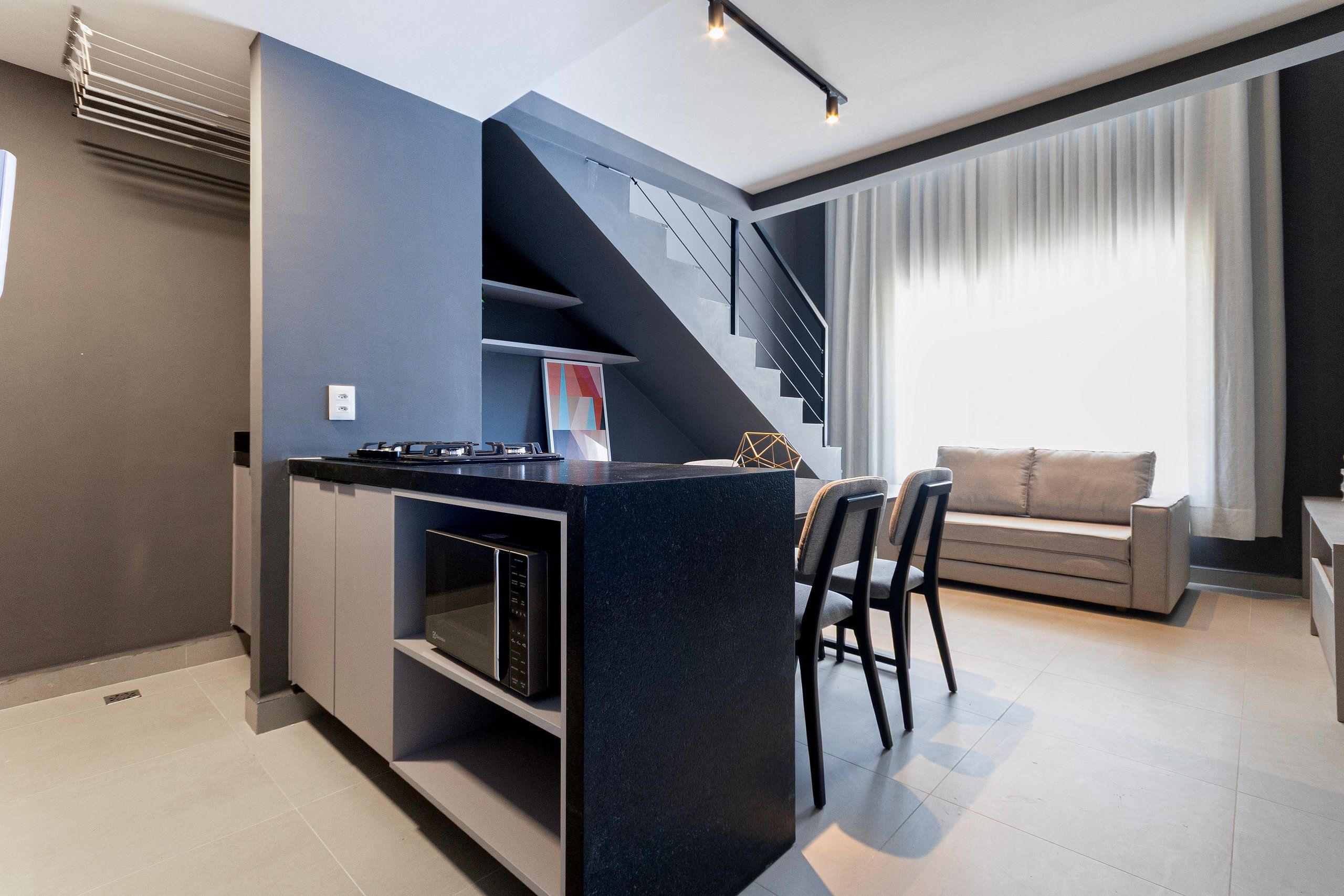 A modern kitchen with a built-in island, a dining area with a sofa and chairs, and a staircase leading to an upper level.