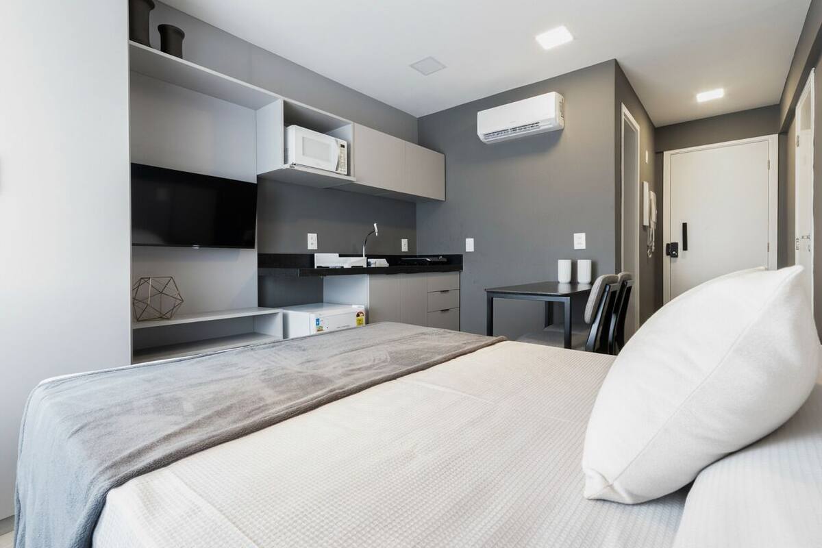 A modern hotel room with a bed, a small desk, a microwave, and a TV.