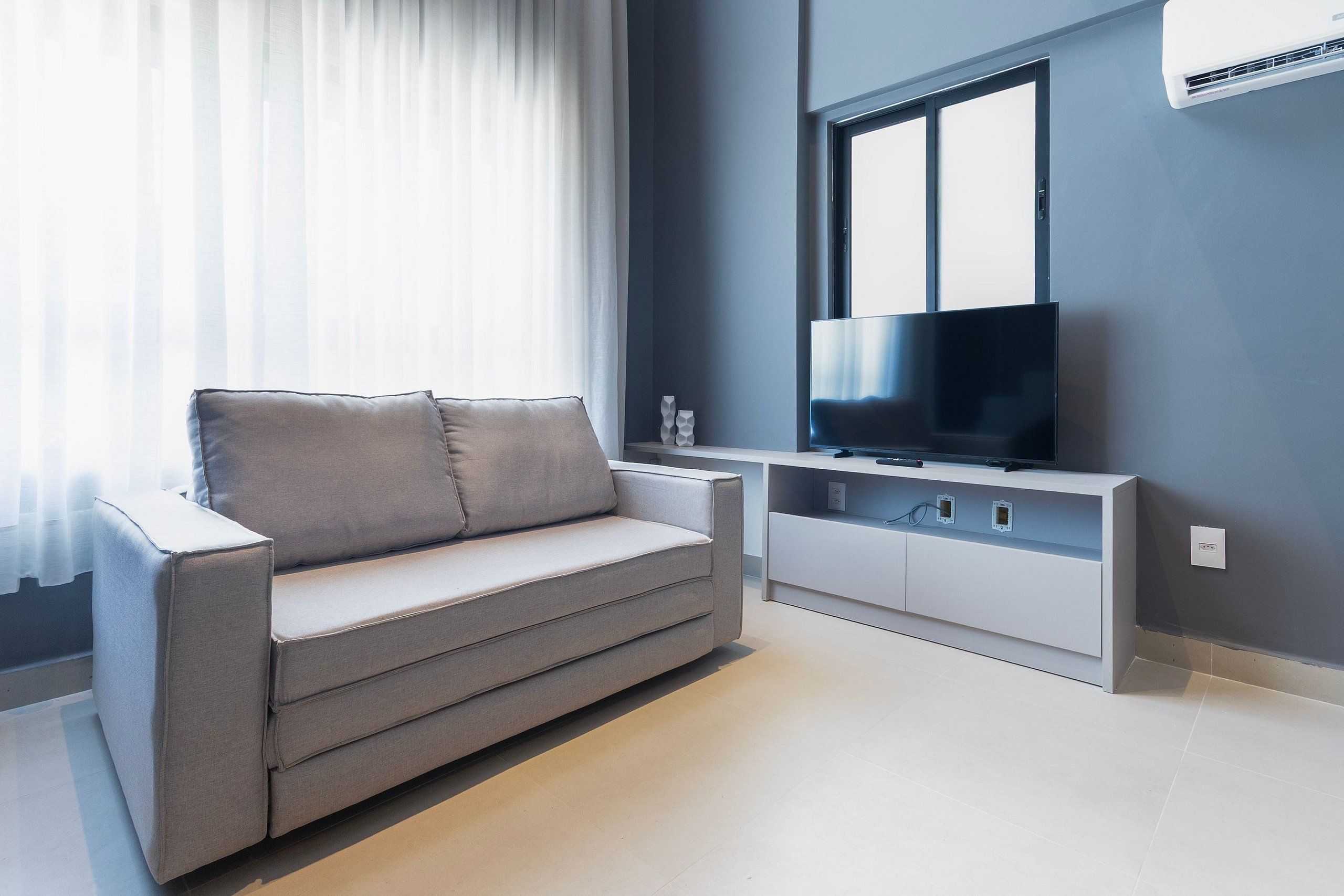 A modern living room with a sofa, a flat-screen TV, and a window with curtains.