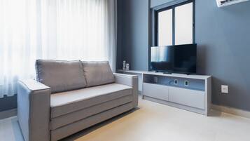 A modern living room with a sofa, a flat-screen TV, and a window with curtains.