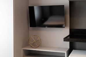 Un televisor de pantalla plana montado en la pared, un adorno geométrico en un estante inferior, y una encimera negra a la derecha.
