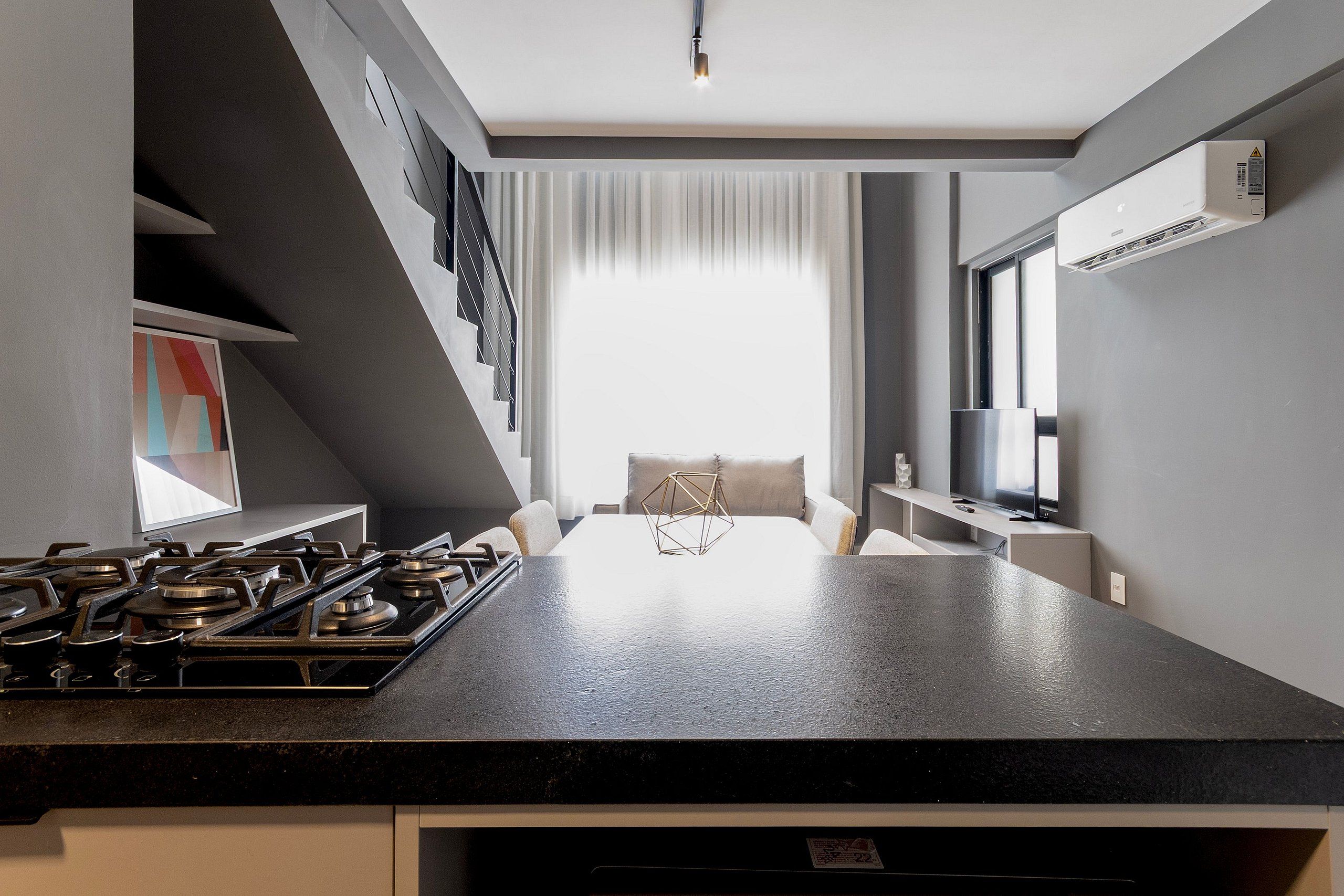 Una cocina moderna con estufa a gas, un comedor con un centro geométrico y un amplio ventanal con cortinas.