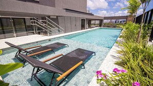 A swimming pool with lounge chairs, stairs, and a view of the city skyline. - Living Tirol Housi Smart Living by Carpediem (Natal)