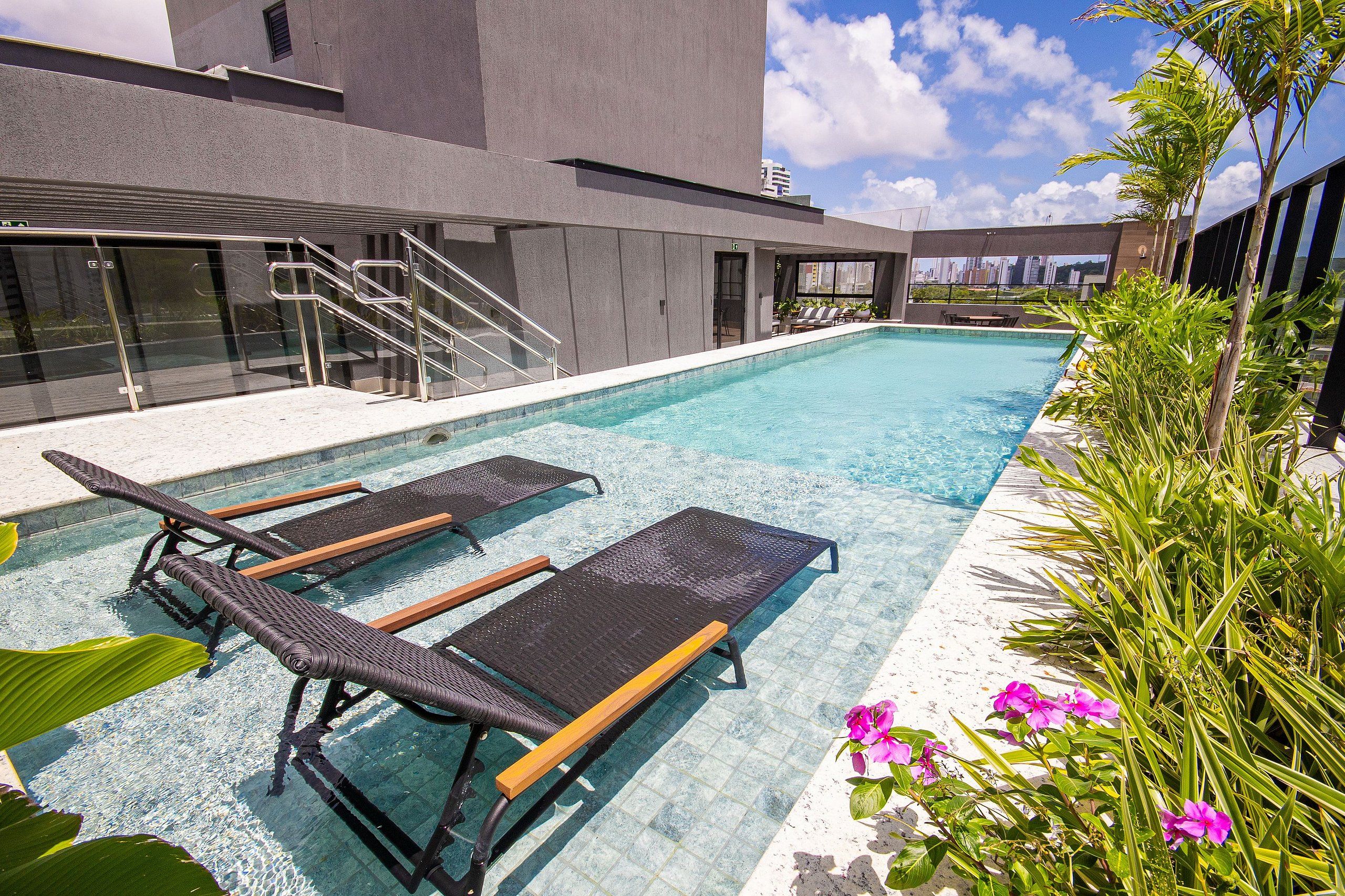 A swimming pool with lounge chairs, stairs, and a view of the city skyline.