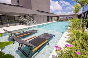 A swimming pool with lounge chairs, stairs, and a view of the city skyline. - Living Tirol Housi Smart Living by Carpediem (Natal)