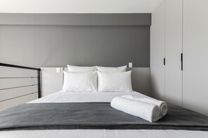 Un dormitorio moderno con una cama, paredes grises y un cabecero blanco.
