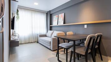 A modern living room with a sofa, dining table, and chairs, a TV, and a plant.