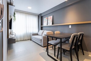 Una sala de estar moderna con sofá, mesa de comedor, sillas, televisor y una planta.
