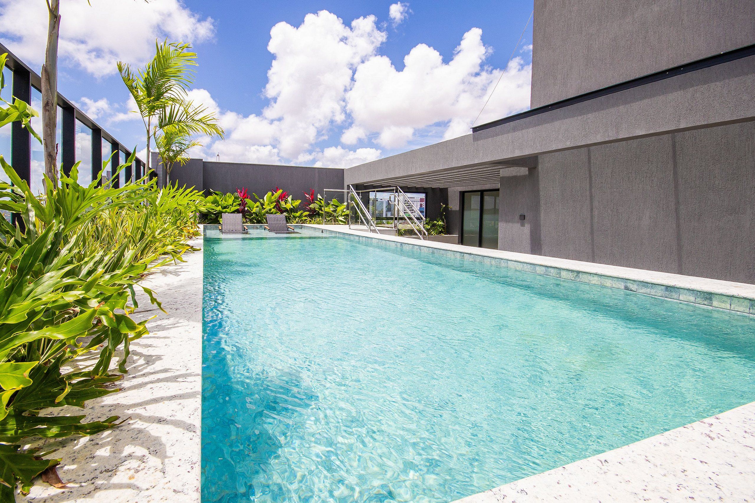 Una piscina con agua cristalina azul, rodeada de plantas y un edificio moderno.