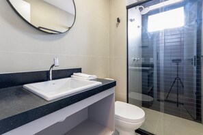 Une salle de bain moderne avec un lavabo blanc, des toilettes et une douche séparée par une paroi de verre.