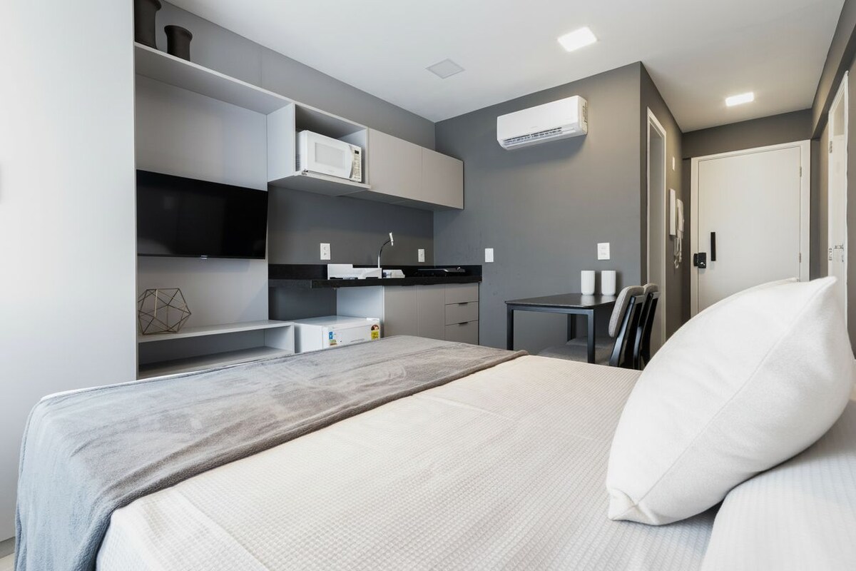 Une chambre d’hôtel moderne équipée d’un lit, d’un petit bureau, d’un four à micro-ondes et d’une télévision.