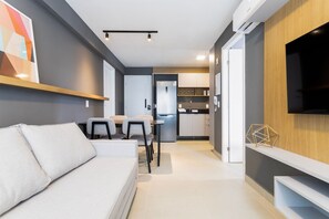 Una sala moderna con un sofá, una mesa de comedor con sillas, una zona de cocina con armarios y un televisor montado.