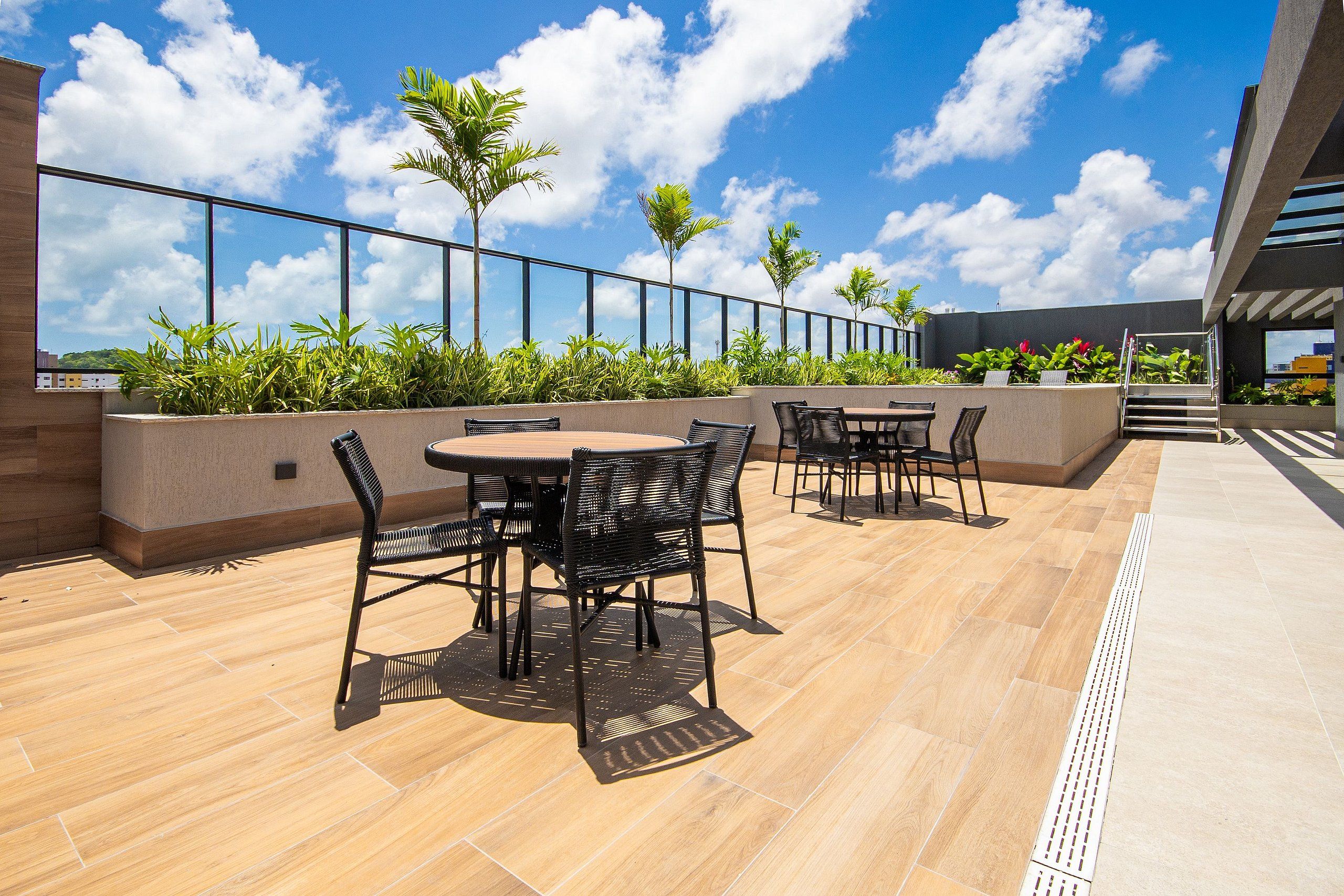 Un patio al aire libre con mesas y sillas, rodeado de plantas y un cielo despejado.