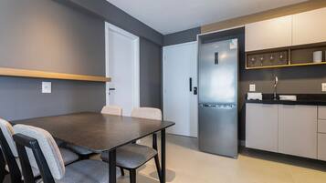 Een moderne keuken met een geïntegreerde koelkast, een eettafel met stoelen en een aanrecht met wijnglazen.