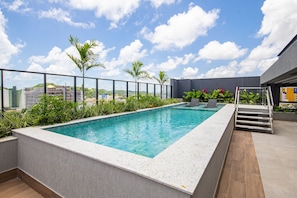 Una piscina en la azotea con vistas despejadas al paisaje urbano, rodeada de vegetación y una estructura de edificio moderna.