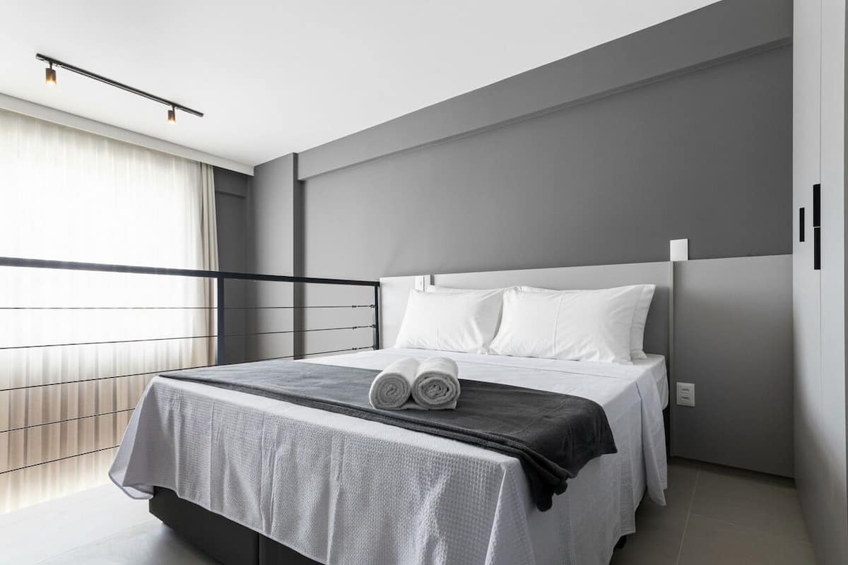 A modern hotel room with a large bed, a balcony, and a view.