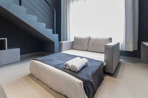 Un dormitorio moderno con una cama, un sofá gris, una escalera y un ventanal con cortinas.