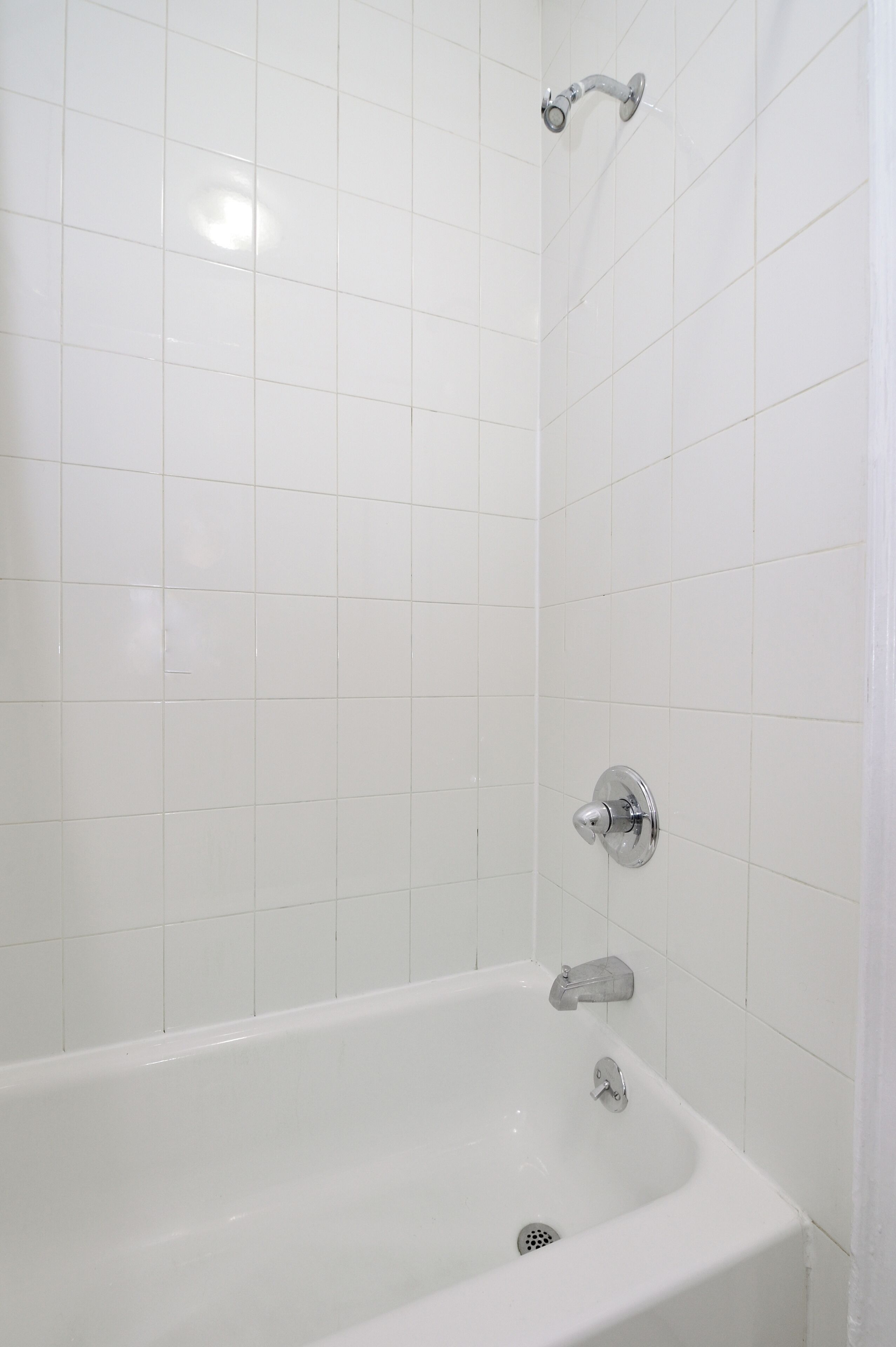 Ein Badezimmer mit weißen Fliesen, einer Badewanne und einer Duschbrause.