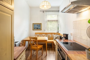 Een kleine keuken met een eettafel, stoelen, een fornuis en een hanglamp.