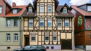 Une maison traditionnelle à colombages, dotée de nombreuses fenêtres et avec une voiture garée devant.