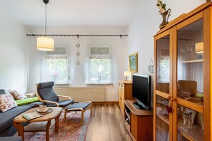 Een woonkamer met een bank, twee fauteuils, een salontafel, een televisie en een kast met glazen deuren.