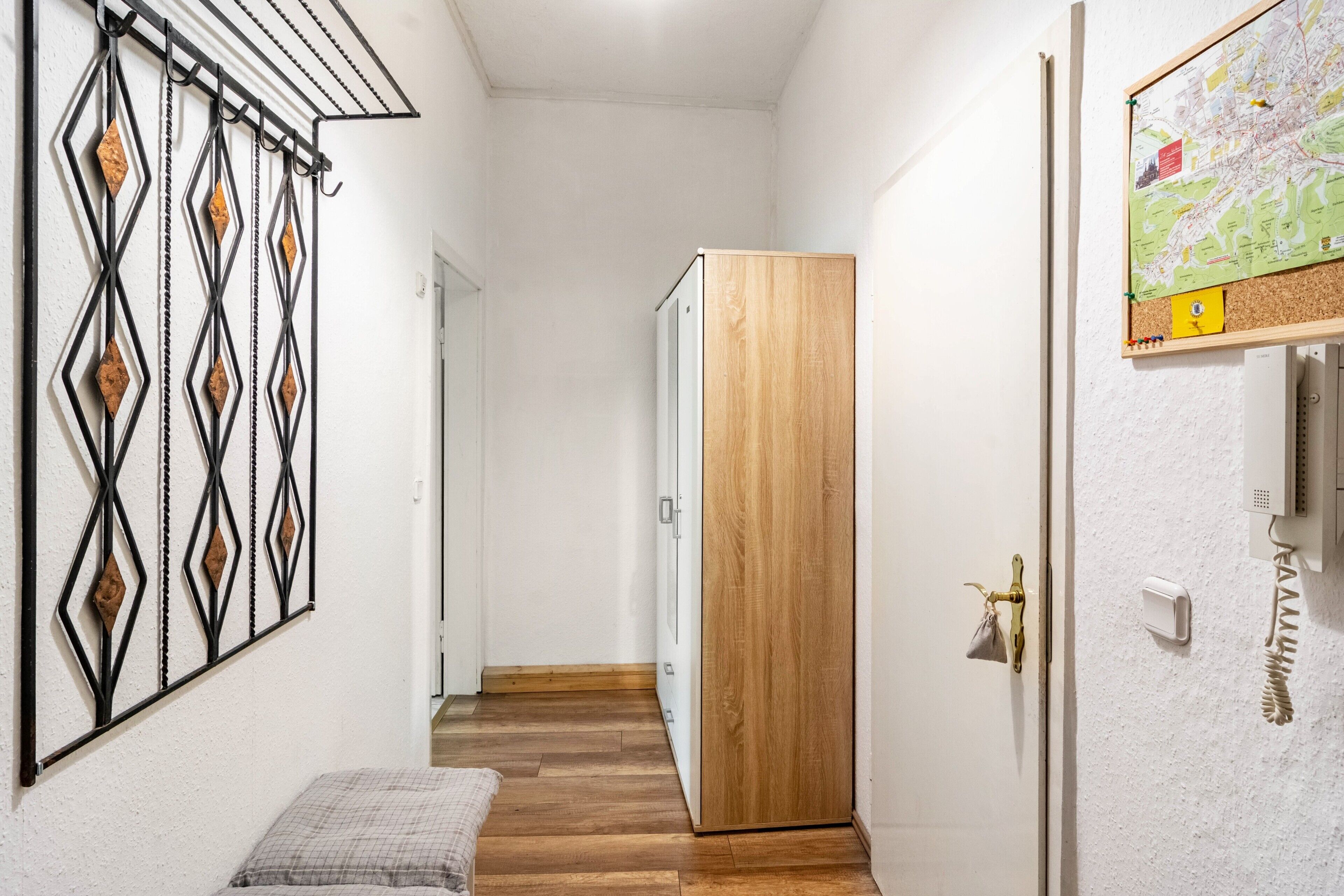 A hallway with a wooden door, a metal gate, a small bench, and a wall-mounted map.