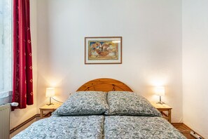 Une chambre à coucher avec une tête de lit en bois, deux lampes de chevet, un lit avec une literie à motifs, une fenêtre avec des rideaux rouges et un tableau encadré accroché au mur.