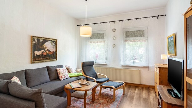 Un salon avec un canapé, des fauteuils, une table basse, un téléviseur et un tableau au mur.