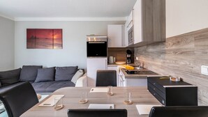 A modern kitchen with a built-in oven, a dining area with a table and chairs, and a gray sofa in the living area. - Apartment for 6 Guests (57 m²) with Private Terrace and Wi-Fi (Kalkhorst)