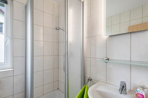 Un baño con cabina de ducha de vidrio, un lavamanos, un espejo y una ventana.