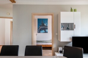 A room with a bed, a dining table with chairs, a white cabinet with pictures, and a painting of the Eiffel Tower. - Apartment for 6 Guests (57 m²) with Private Terrace and Wi-Fi (Kalkhorst)
