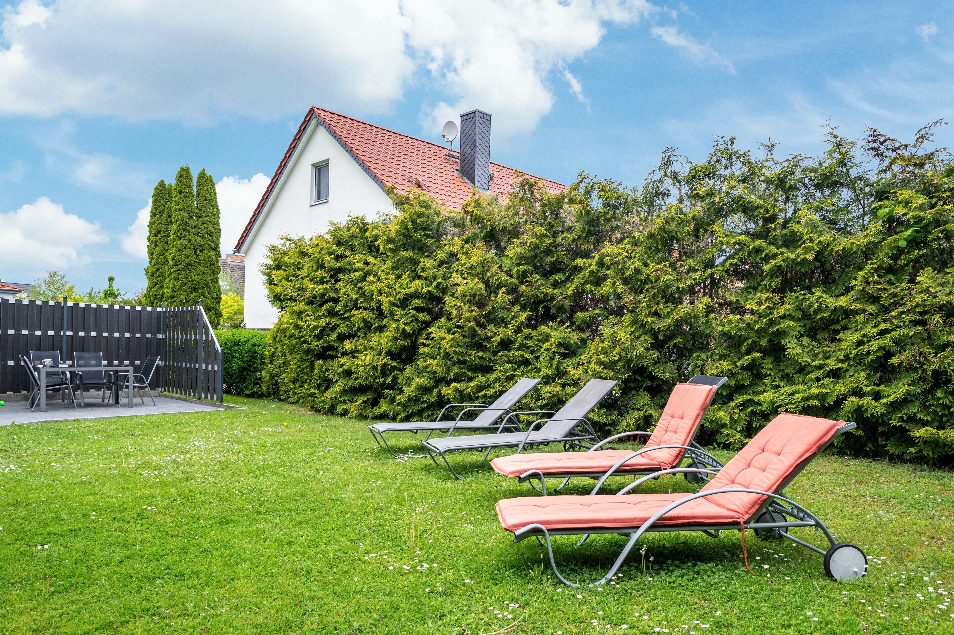 Ein Haus mit rotem Dach, Schornstein und Satellitenschüssel. Drei Liegestühle befinden sich im Vorgarten.