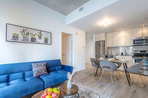 A modern living room with a blue sofa, a dining area with grey chairs, and a kitchen with stainless steel appliances. - Square Victoria - Balcony View & Free Parking (Montreal)