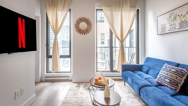 Una sala de estar moderna con un sofá azul, un televisor de pantalla plana y un amplio ventanal con cortinas.