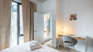 Una habitación de hotel con cama, escritorio, silla, un cuadro y vistas al exterior.