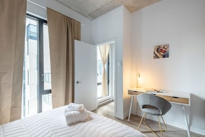 A hotel room with a bed, a desk, a chair, a painting, and a view of the outside. - Square Victoria - Balcony View & Free Parking (Montreal)