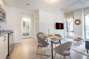 A modern kitchen with a dining area, a TV mounted on the wall, and a view through the window. - Square Victoria - Balcony View & Free Parking (Montreal)