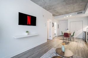 A modern living space with a mounted TV displaying a red 'N', a dining area with a table and chairs, and a small plant on a shelf. - Modern 1BR in Old Montreal + Lounge Access (Montreal)