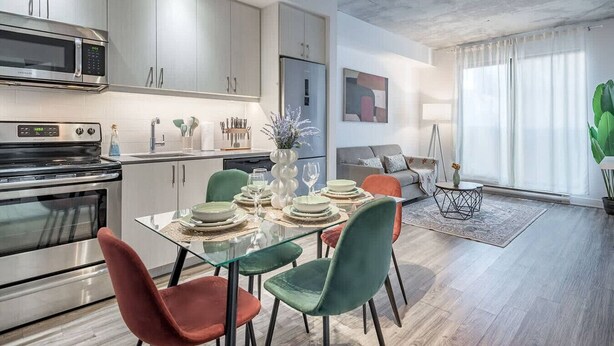 A modern kitchen with stainless steel appliances, a dining area with a glass table and chairs, and a living area with a sofa and a large window. - Modern 1BR in Old Montreal + Lounge Access (Montreal)