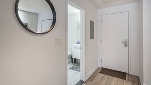 A hallway with a round mirror, a white door, and a view into a bathroom. - Modern 1BR in Old Montreal + Lounge Access (Montreal)