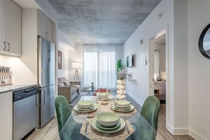 A modern kitchen with stainless steel appliances, a dining area with a glass table and green chairs, and a living room with a sofa and a TV. - Modern 1BR in Old Montreal + Lounge Access (Montreal)