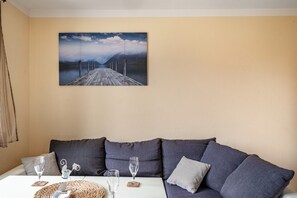 A room with a grey sofa, a table with glasses and coasters, and a painting of a pier.