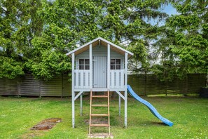 Ein Spielhaus aus Holz mit Rutsche und Leiter.