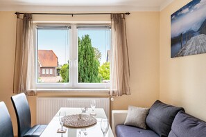 Ein Zimmer mit Esstisch für zwei Personen, einer Couch, einem Fenster mit Vorhängen und einem Gemälde an der Wand.