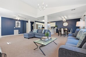 Ein modernes Wohnzimmer mit einer Eckcouch, einem Glastisch und einem Essbereich mit rundem Tisch und Stühlen.