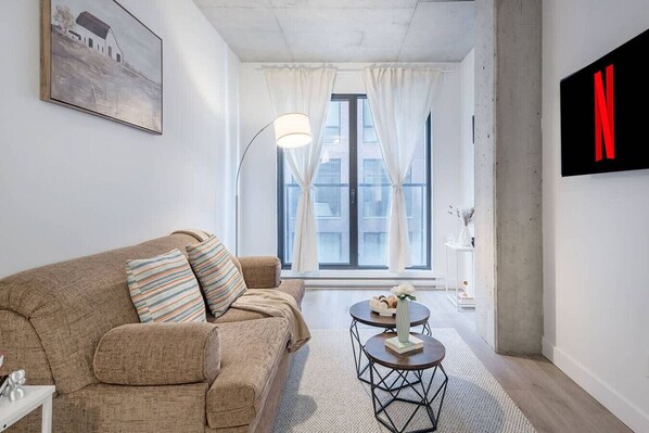 Ein modernes Wohnzimmer mit einer Couch, einem runden Couchtisch und einem großen Fenster mit Vorhängen.