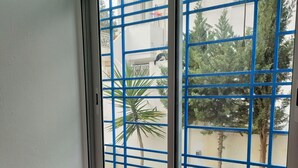 Een kamer met een roze bank, een witte stoel en een raam met blauwe metalen tralies.