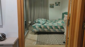 Een slaapkamer met een bed, nachtkastje, stoel, een kamerbreed tapijt met patroon, en een hanglamp.