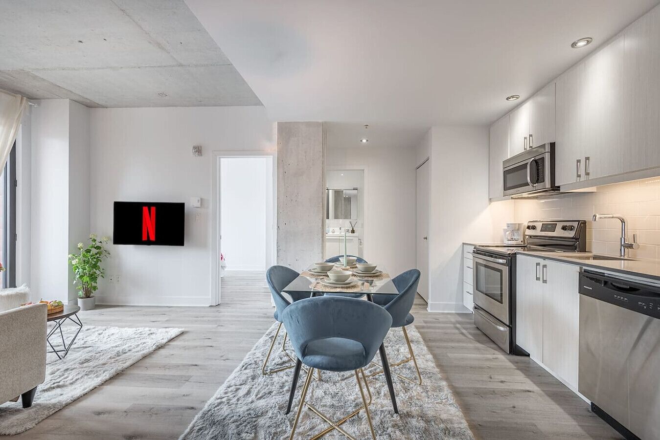 A modern kitchen with stainless steel appliances, a dining area with a table and chairs, and a flat-screen TV mounted on the wall.
