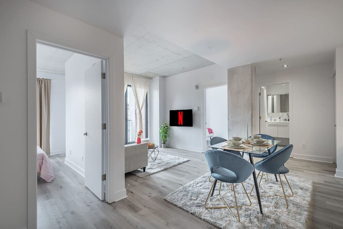 A modern interior with a dining area, a TV mounted on the wall, and a visible kitchen area.